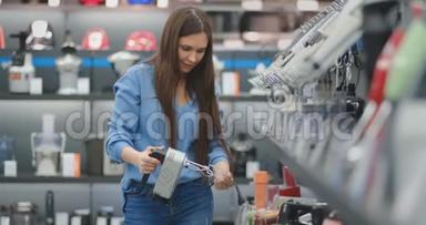 穿蓝色衬衫的年轻漂亮女孩在电器商店里选择搅拌机